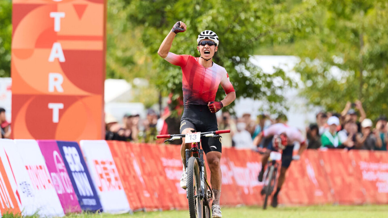 A mountain-bike rider celebrating at the finish during the 2026 Aichi-Nagoya Asian Games in an official Games photograph