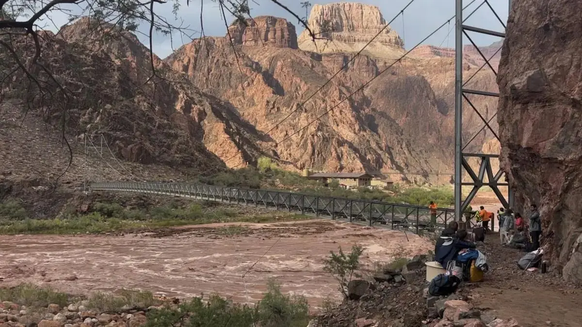 People wait near a bridge while a helicopter operates during flooding in Grand Canyon National Park