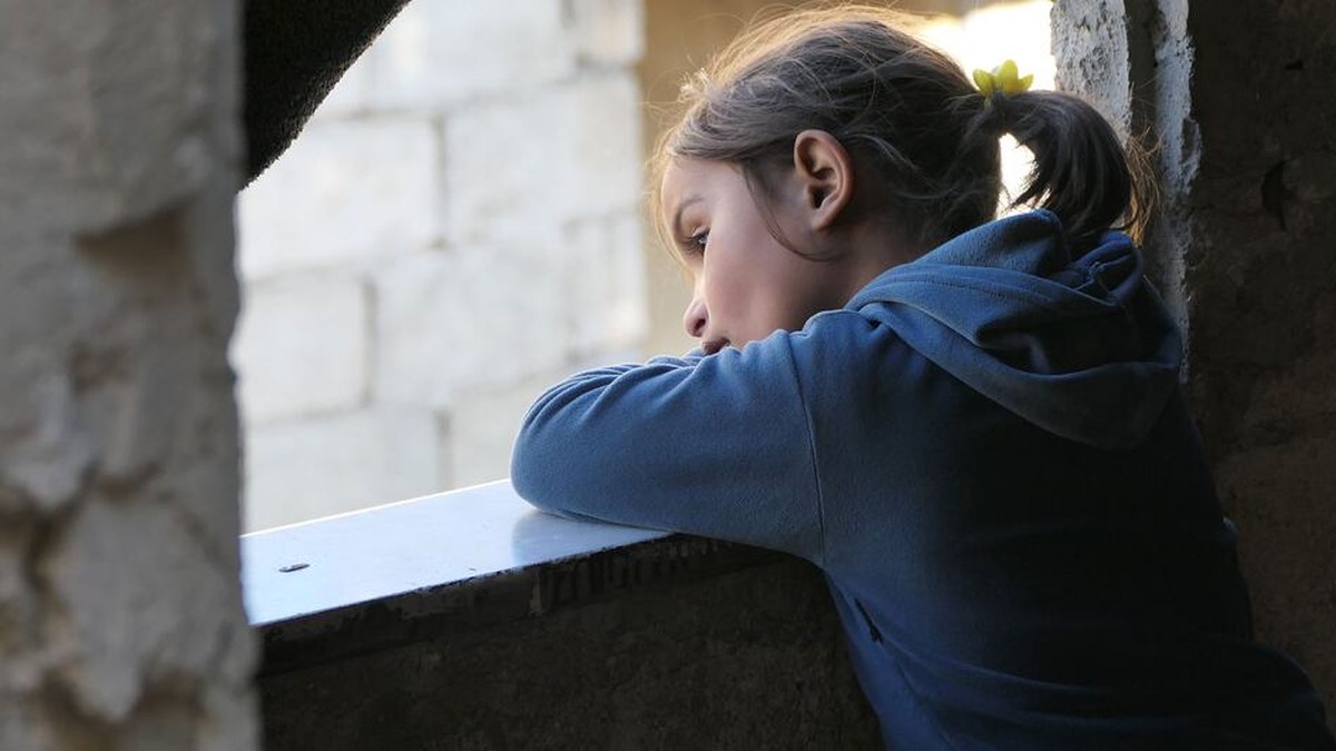 A young girl looks out from a dim room in Aleppo, Syria