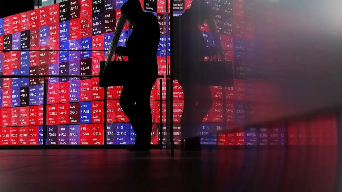 A person walks past an electronic market board displaying Japanese stock prices in Tokyo