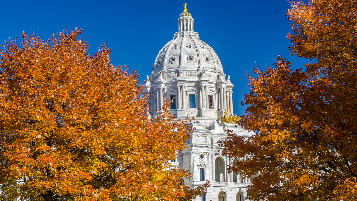 The Minnesota State Capitol framed by orange autumn trees under a clear blue sky